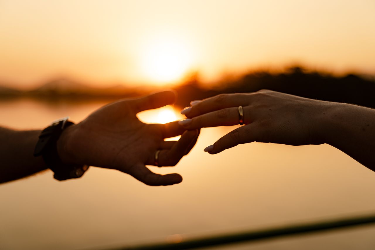 Silhouette of hands touching against a warm sunset, highlighting intimate connection.